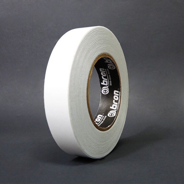 A single roll of 1 inch double sided film tape standing in front of a grey background