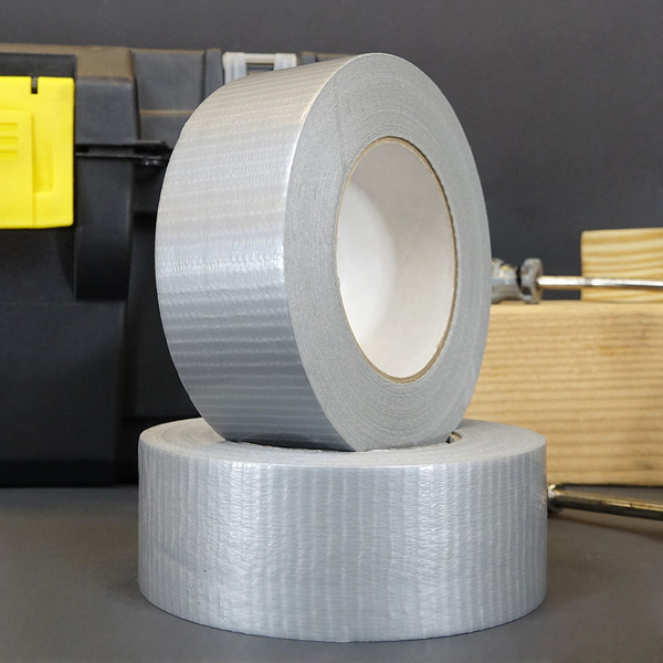 Two rolls of silver utiility grade duct tape stacked on each other in front of a toolbox and wood planks