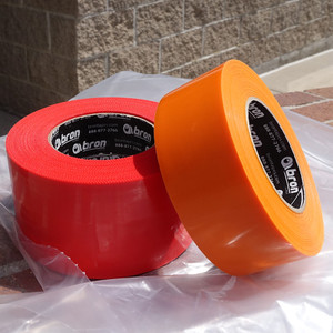 Roll of red and orange polyethylene tape on piece of plastic sheeting outdoors