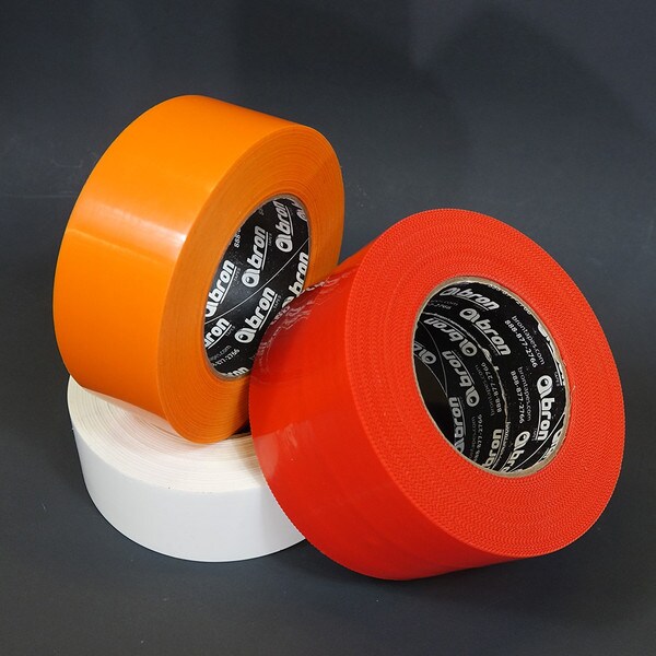 Rolls of red, white, and orange polyethylene tape stacked on black background