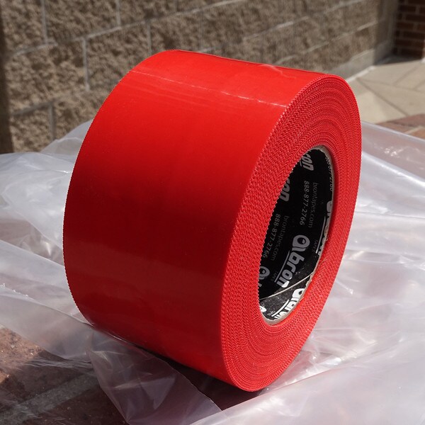 Roll of red polyethylene tape outside on a piece of plastic sheeting