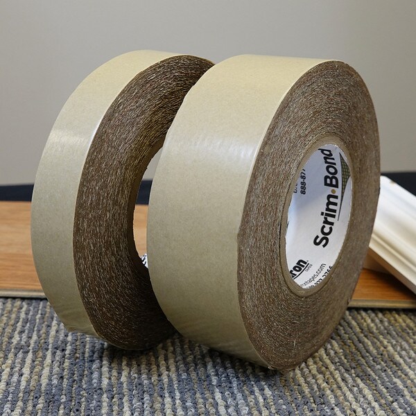 Two rolls of Scrim-Bond scrim tape shown on top of carpet remnant with flooring materials in background