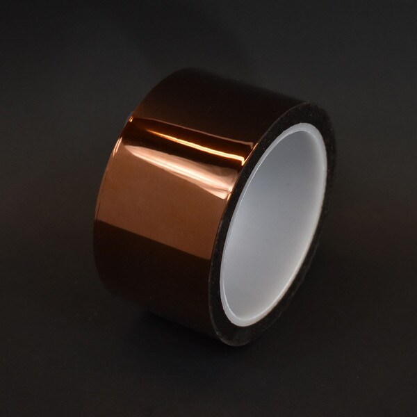 Two inch roll of polyimide tape with white plastic core in front of grey background