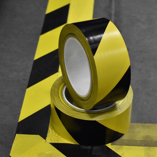 Rolls of black and yellow hazard stripe tape sitting on safety marking in warehouse