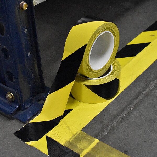 Rolls of black and yellow hazard stripe tape being applied to warehouse floor