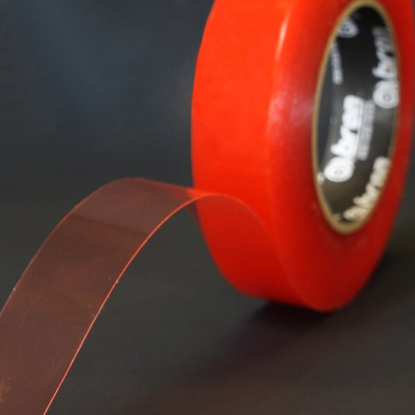 Roll of double sided tape slightly unwound to show adhesive with red carrier