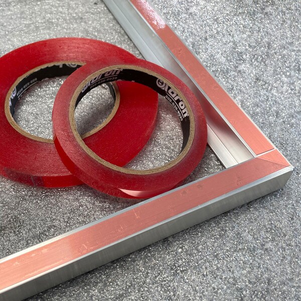 Double sided tape being applied on frames and carrier partially removed to show adhesive being applied