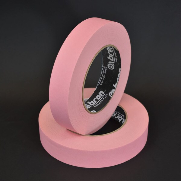 Two rolls of 1 inch pink masking tape stacked in front of black background